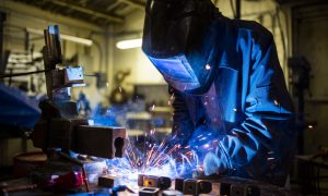 A person welding an item while wearing protective gear.