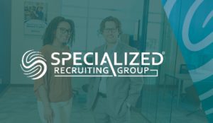 Two professionals standing in an office with the Specialized Recruiting Group logo prominently displayed in the foreground. Text in image says "Specialized Recruiting Group."