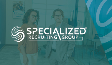 Two professionals standing in an office with the Specialized Recruiting Group logo prominently displayed in the foreground. Text in image says "Specialized Recruiting Group."