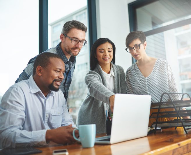 Four people gathered around a laptop in an office.