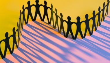 A row of connected black paper figures against a yellow and pink background with shadows cast behind.