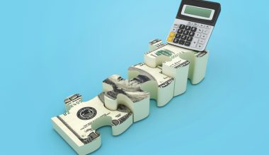 A calculator sits on top of interlocking puzzle pieces designed to look like hundred‑dollar bills against a light blue background.